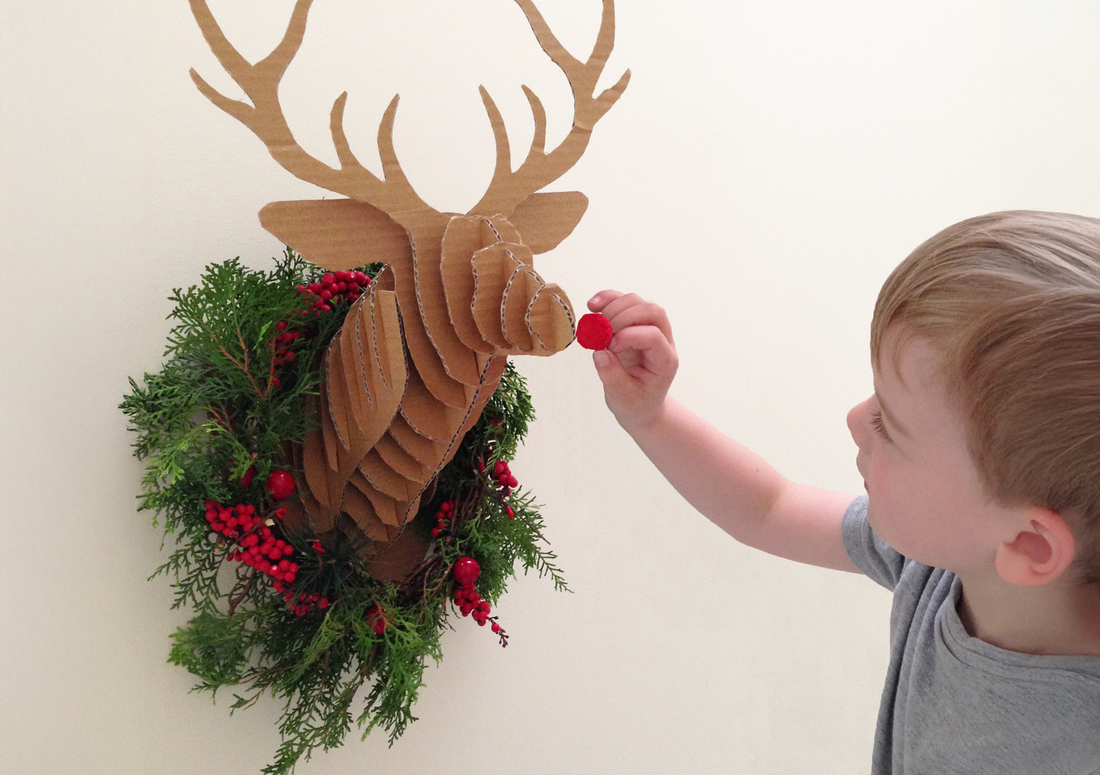 Child sticking a red nose on a DIY Christmas Cardboard Deer Head