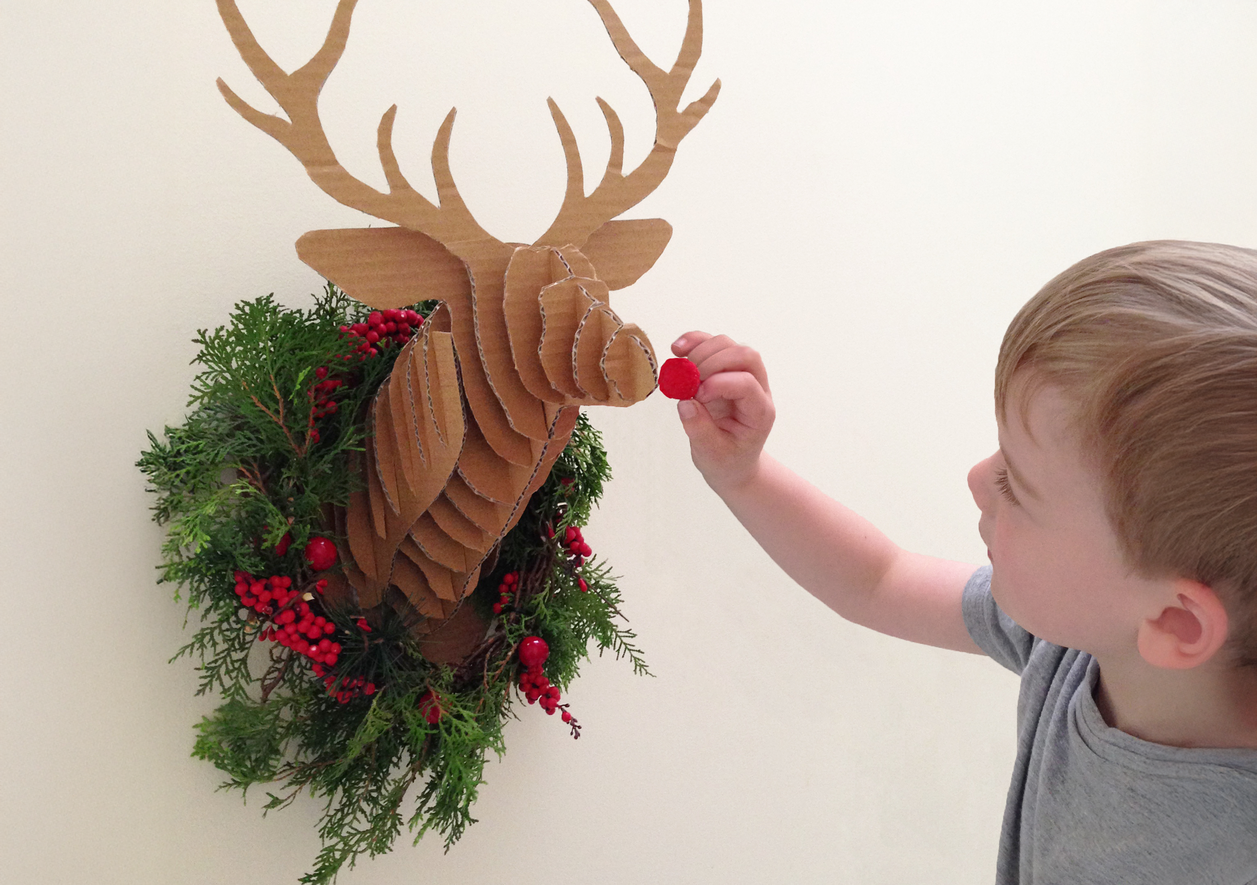 Child sticking a red nose on a DIY Christmas Cardboard Deer Head