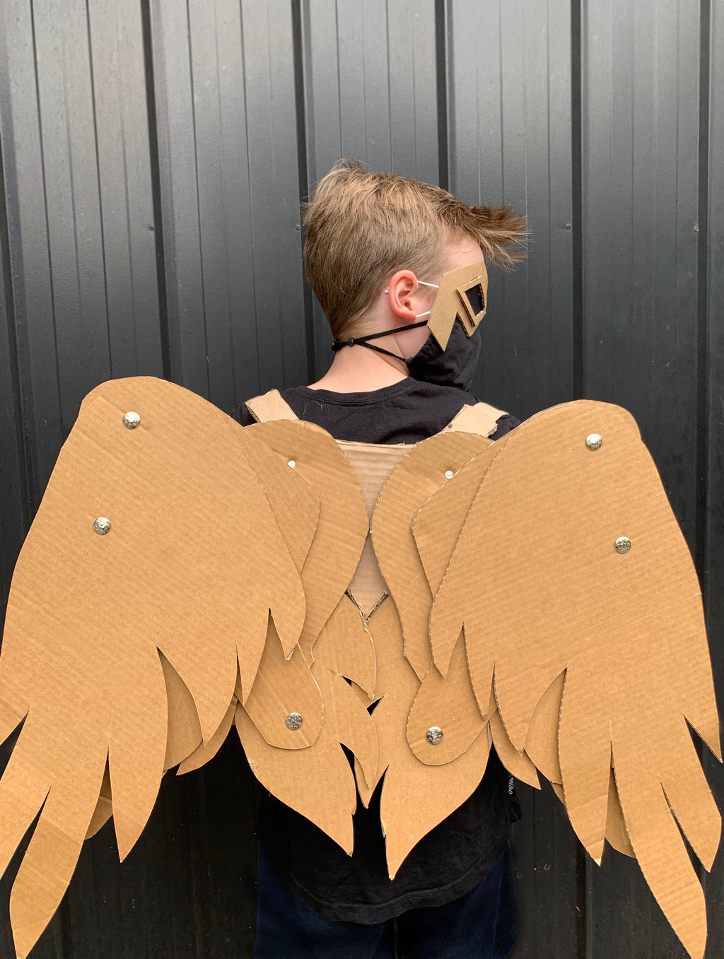 Person wearing cardboard articulating angel wings against a dark background