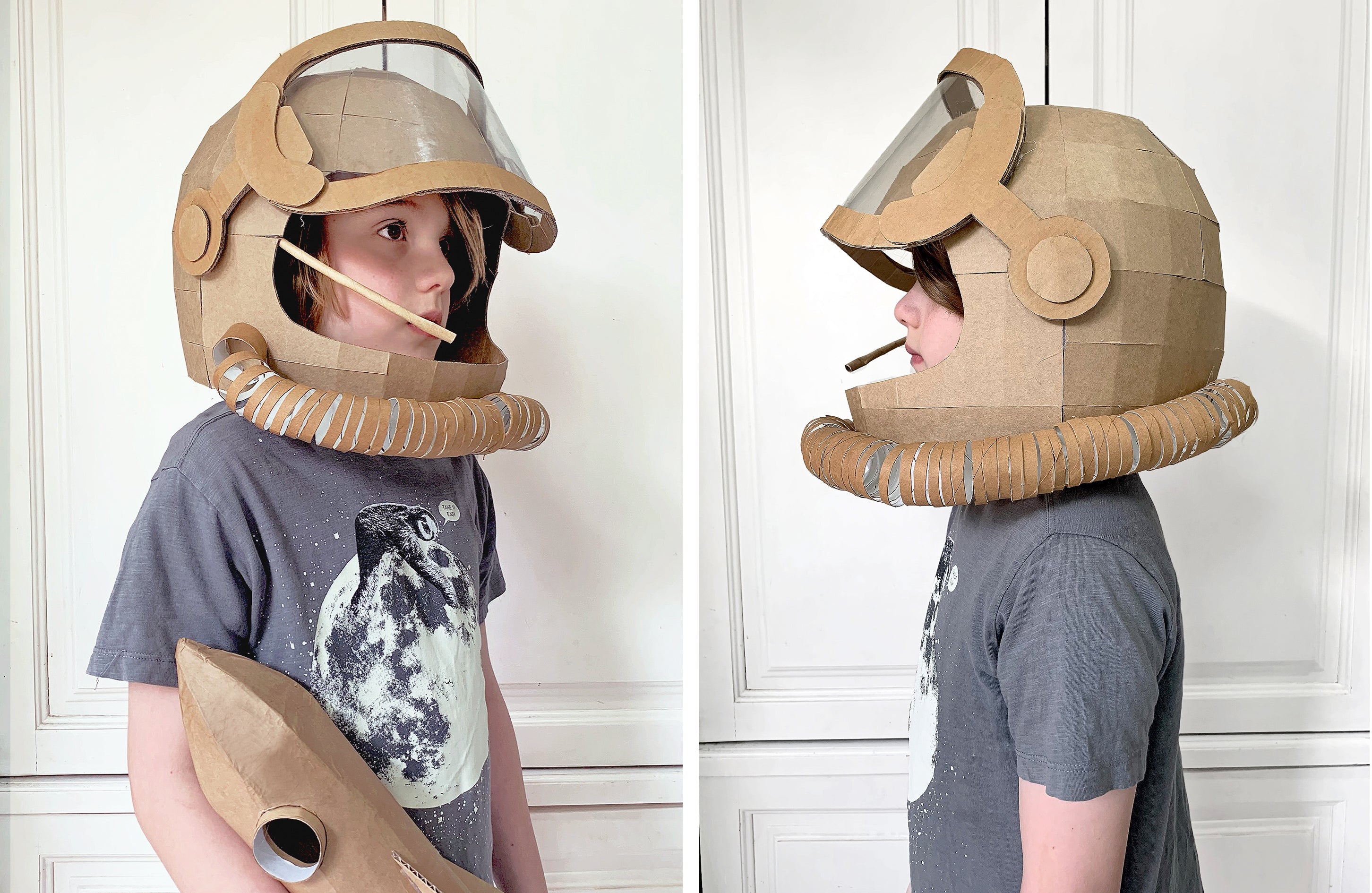 Child wearing a cardboard astronaut helmet with visor and space suit design, standing against a white paneled wall.