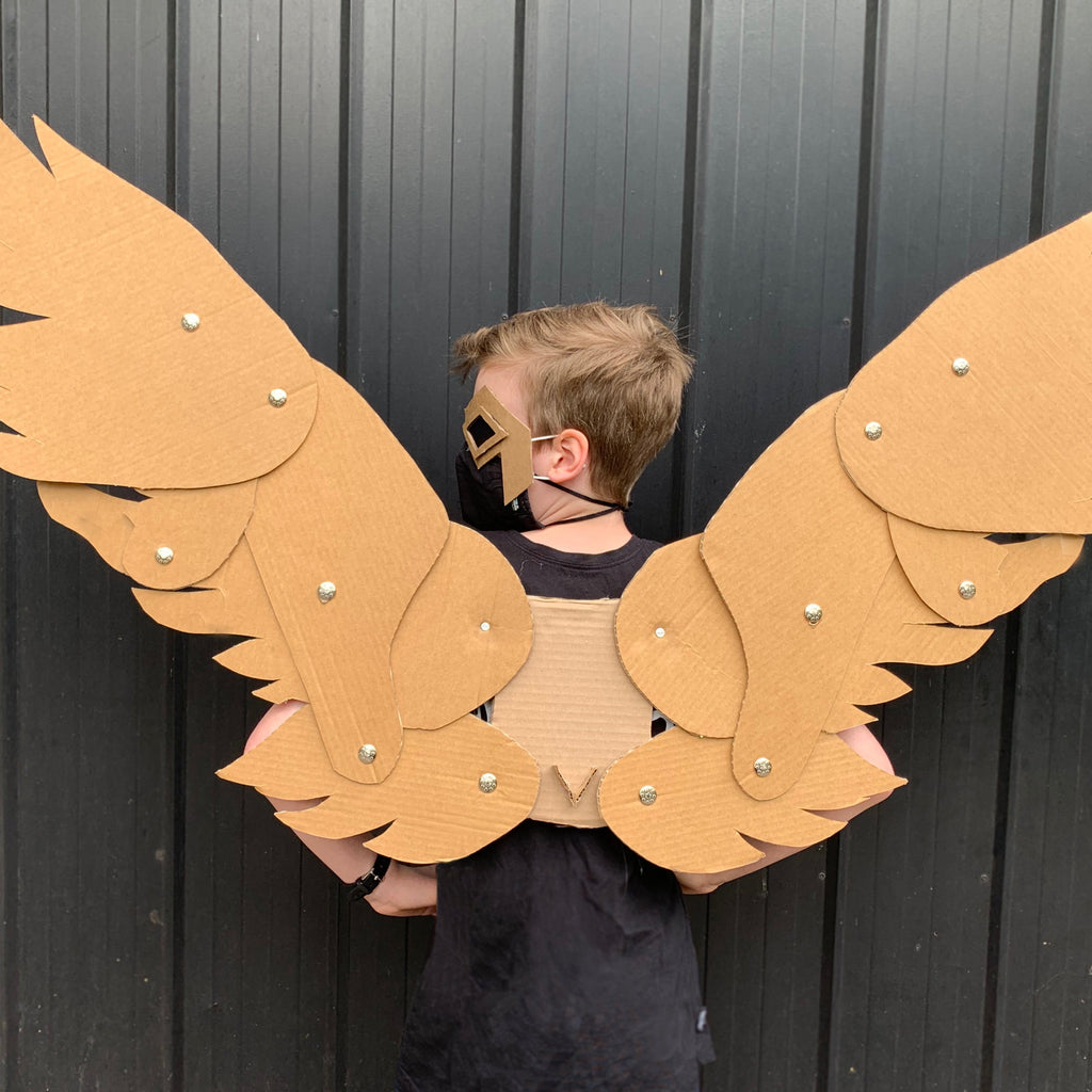 Child wearing cardboard articulating angel wings against a dark background