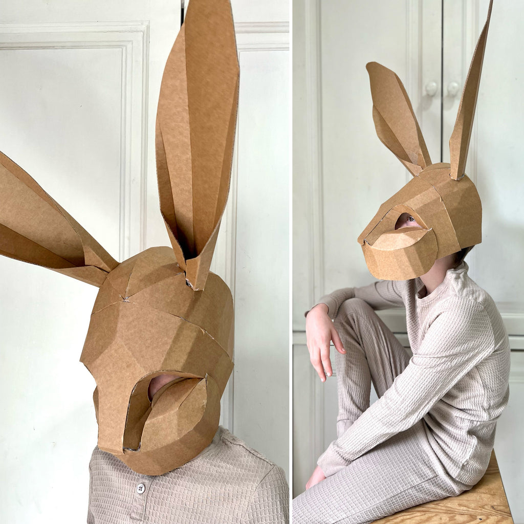 Person wearing a cardboard rabbit mask in two different poses against a white wall.