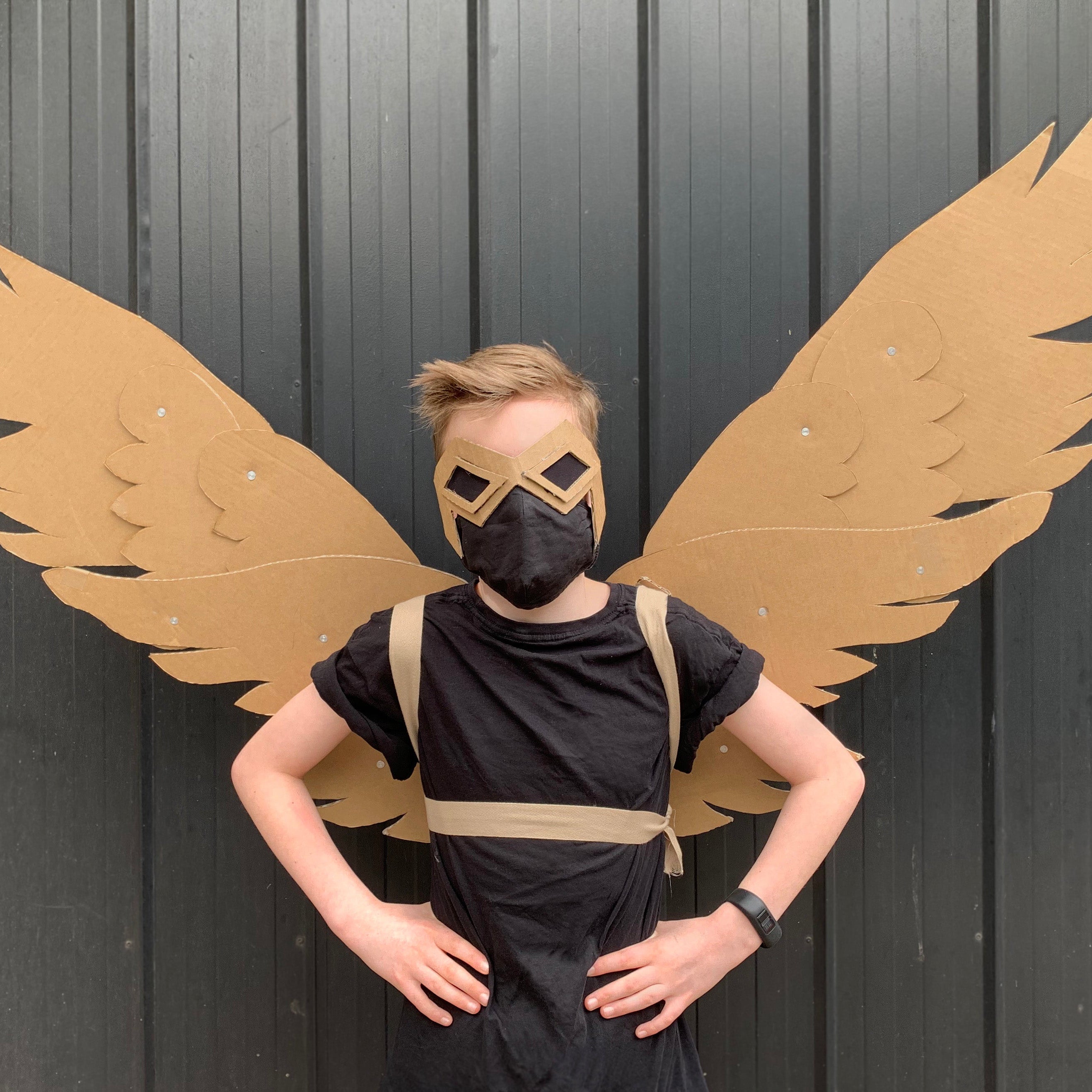 Person wearing a black costume with cardboard wings against a dark background