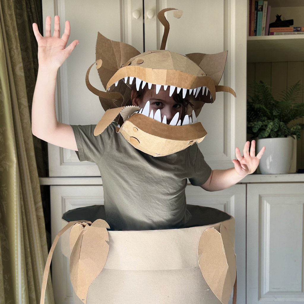 Person wearing a cardboard Audrey 2 inspired costume inside a large beige plant pot
