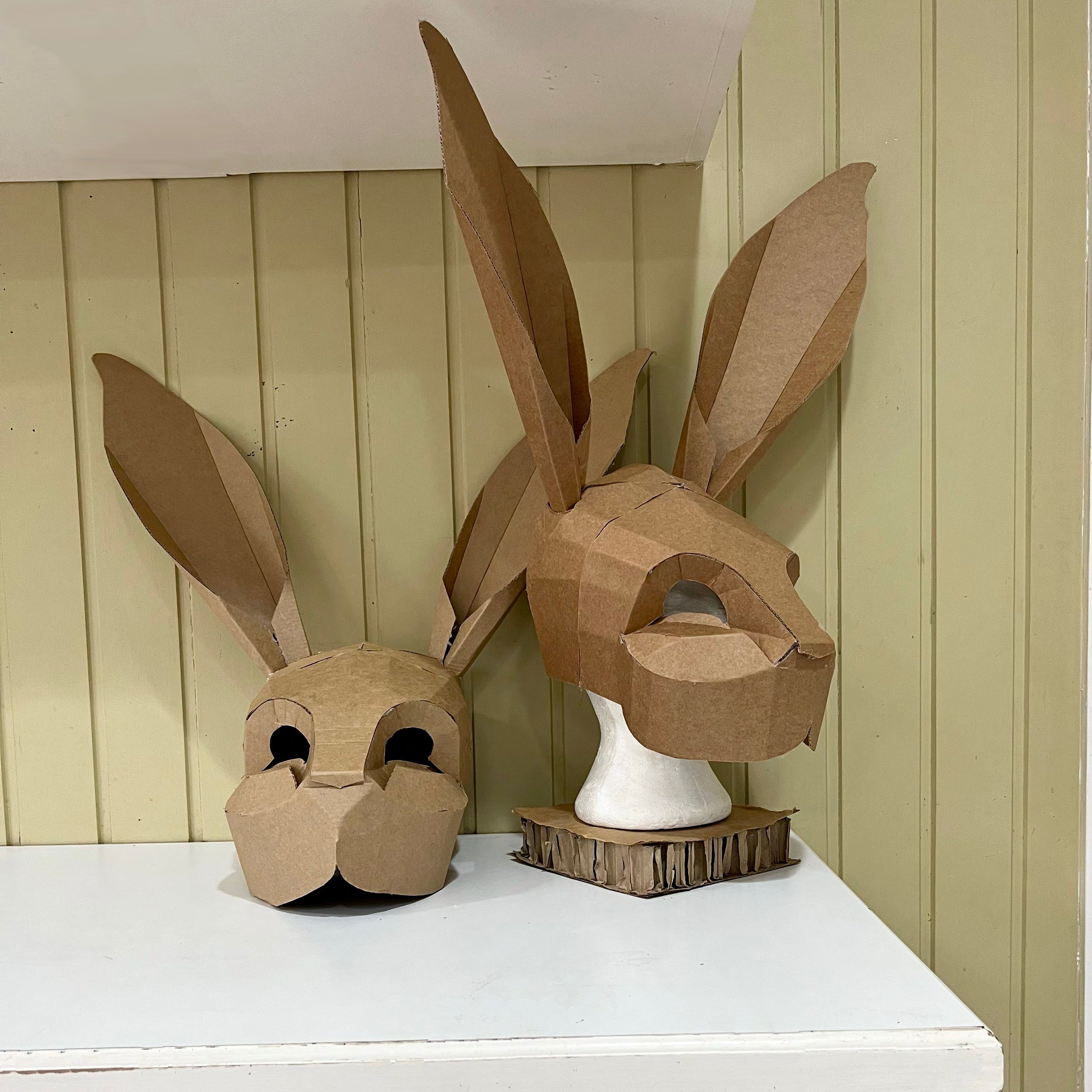 Cardboard rabbit masks on a white surface with a wooden panel background